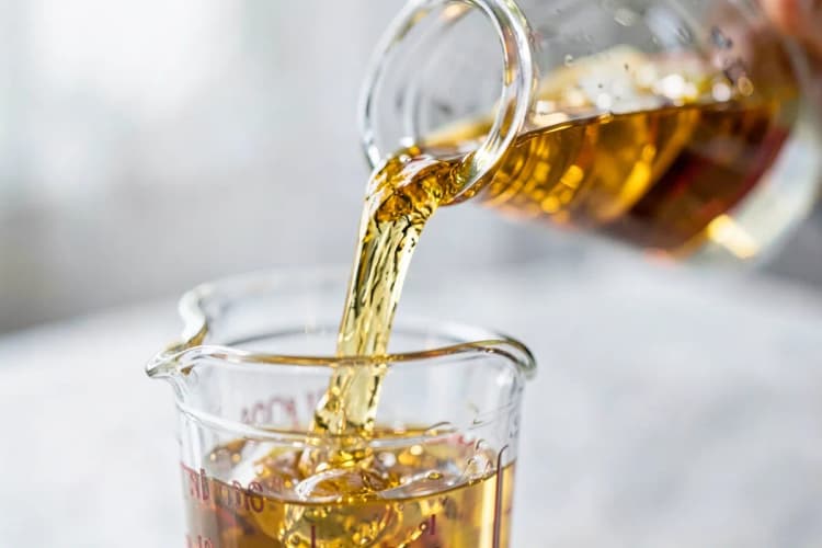 Close-up de um líquido dourado e viscoso sendo derramado de um frasco para um copo medidor.