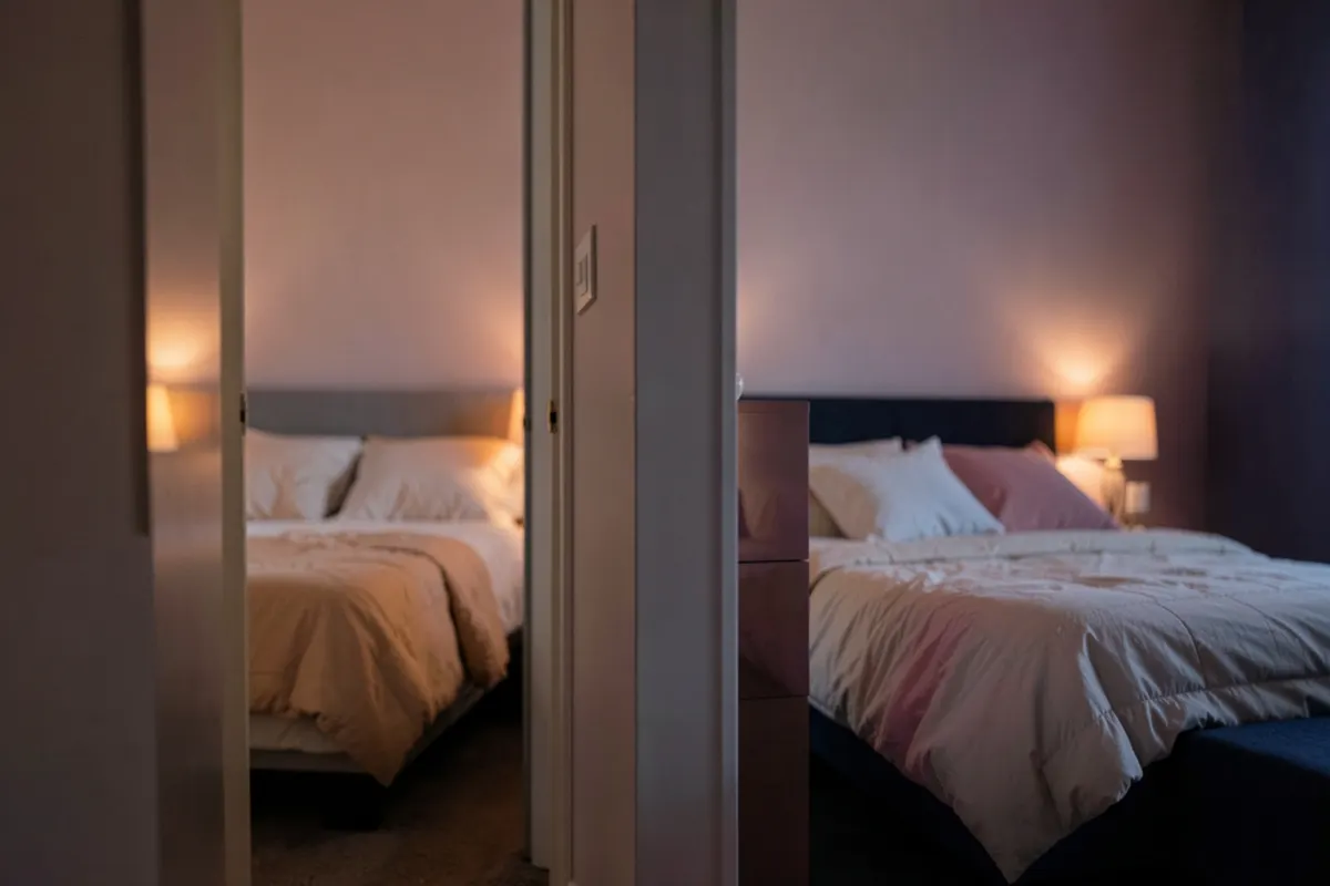Um casal dormindo em camas separadas em quartos diferentes, com uma porta entre eles entreaberta.