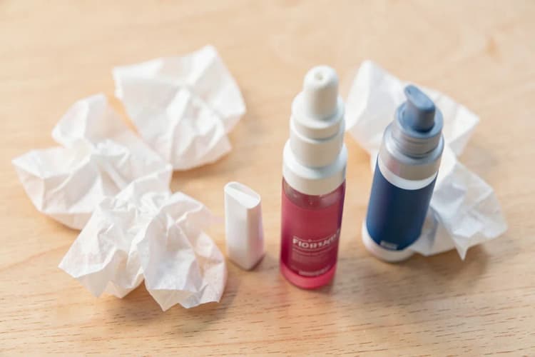 Um conjunto de diferentes tipos de lenços de papel e sprays nasais dispostos sobre uma superfície de madeira clara.