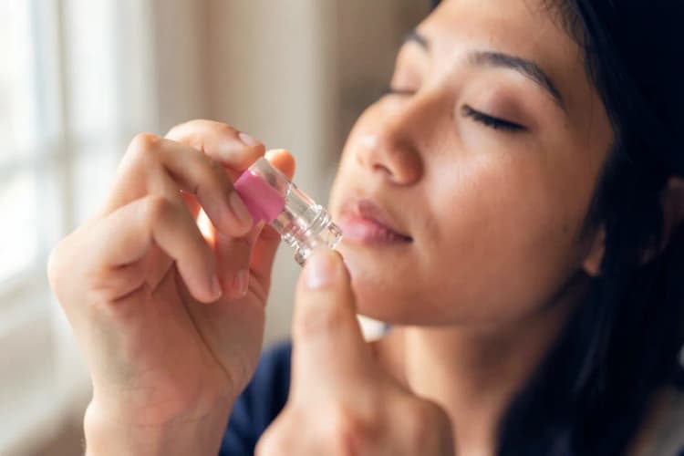 Uma pessoa usando um spray nasal com os olhos fechados, em um ambiente interno com luz suave.