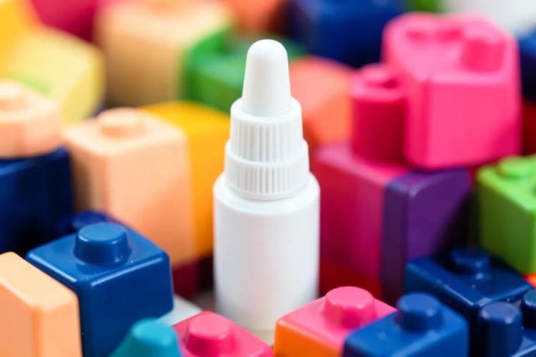 Frasco de spray nasal em miniatura ao lado de brinquedos infantis.
