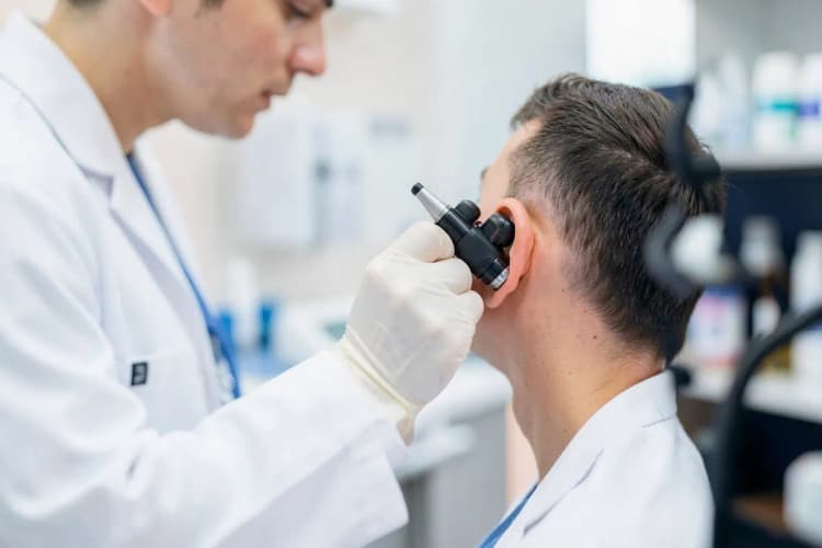 Um médico otorrinolaringologista examinando um paciente com um otoscópio.
